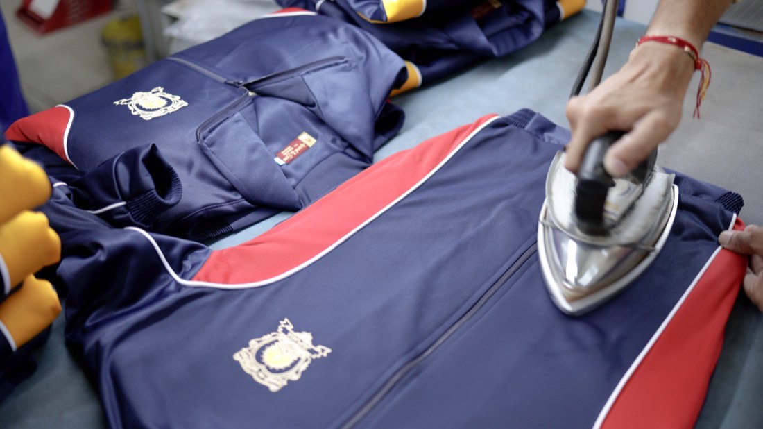 A finished navy garment with an embroidered crest being pressed